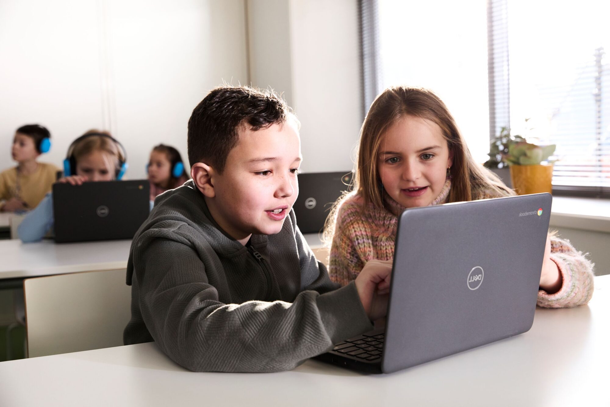 twee kinderen die achter een laptop zitten en iets aanwijzen op het scherm